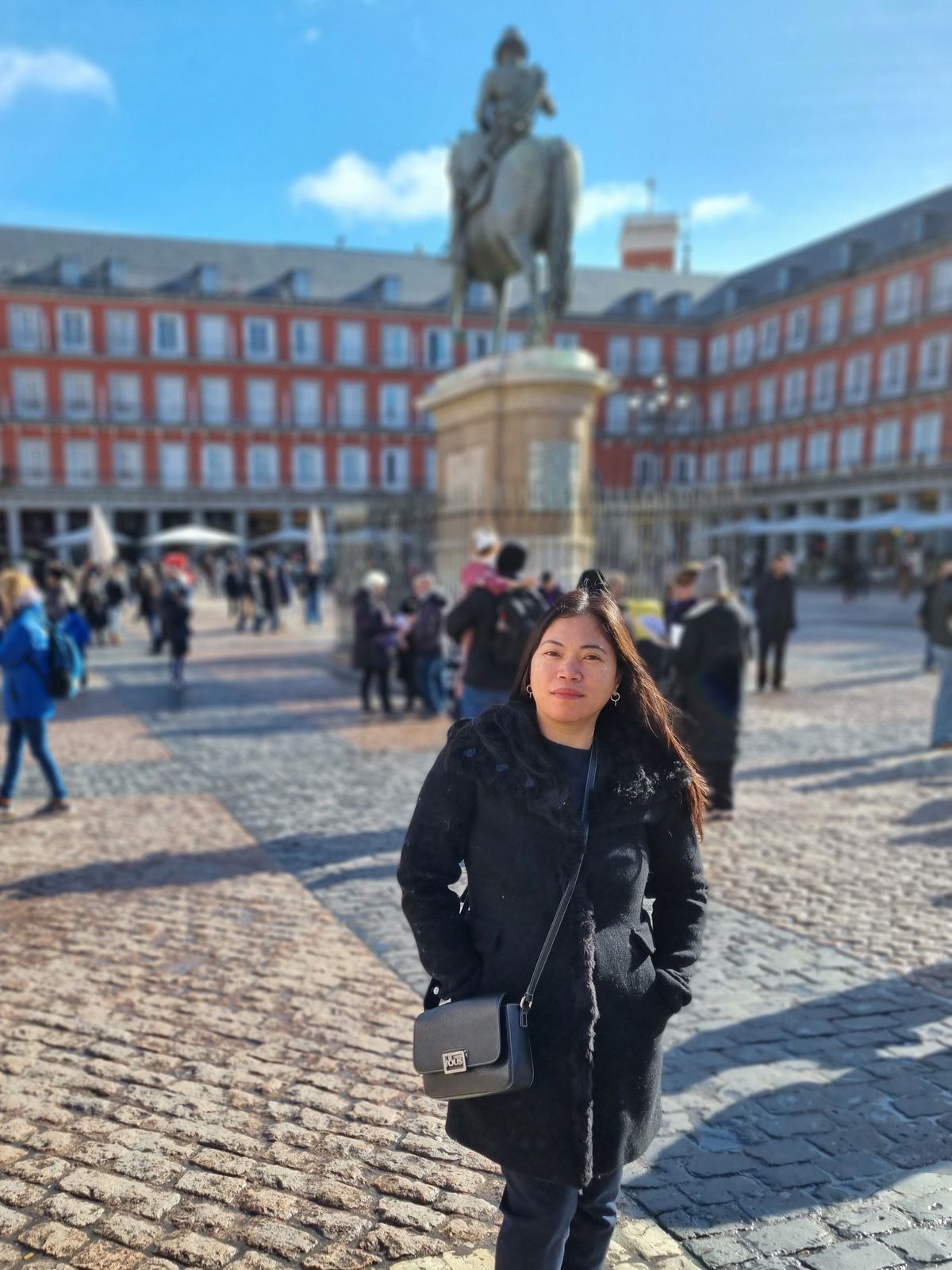 Anselma Benítez smiling in Madrid’s Plaza Mayor, with the equestrian statue and red façades behind her